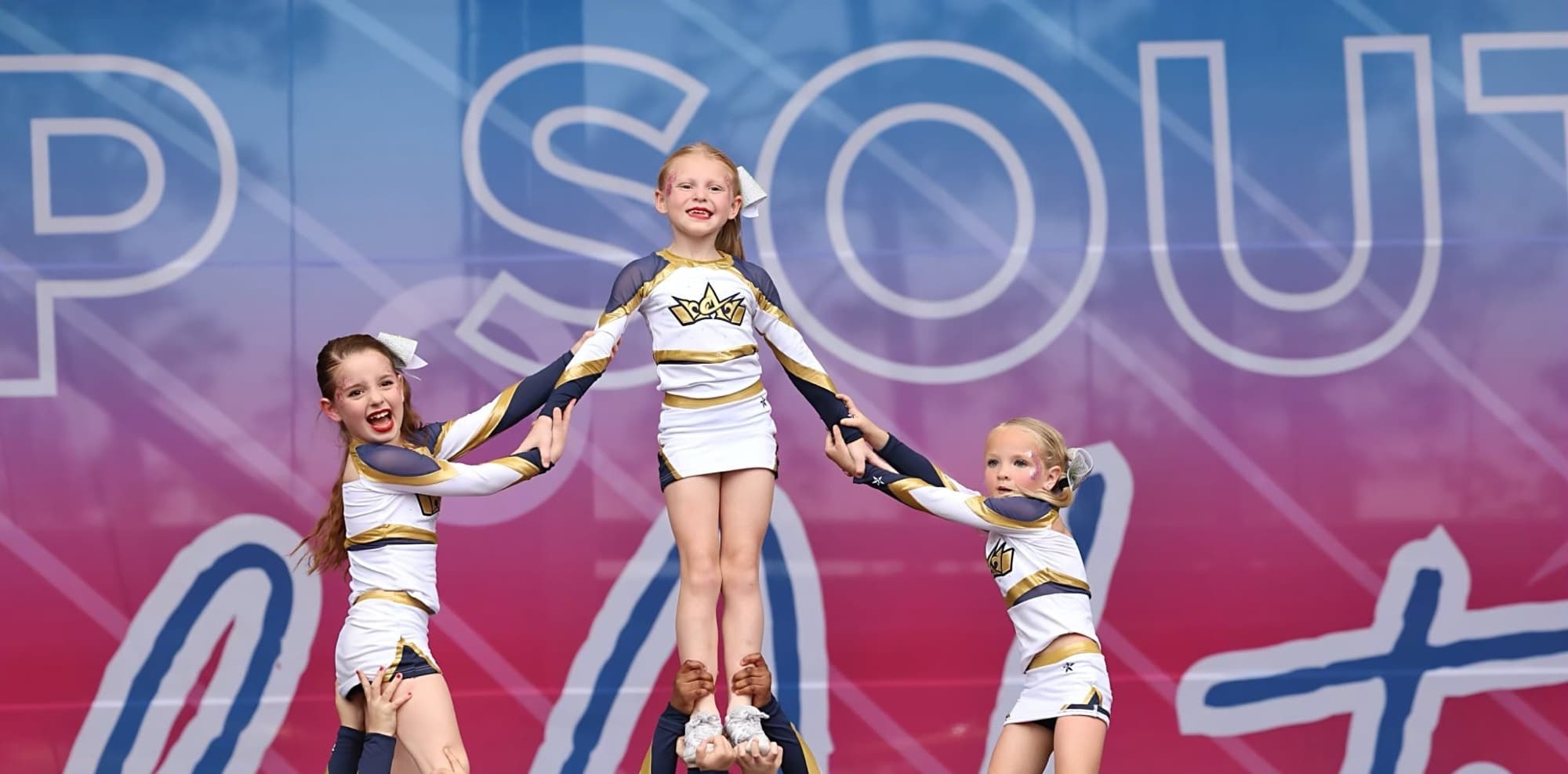 Crown Athletics cheerleaders in navy, gold and white uniforms performing a stunt